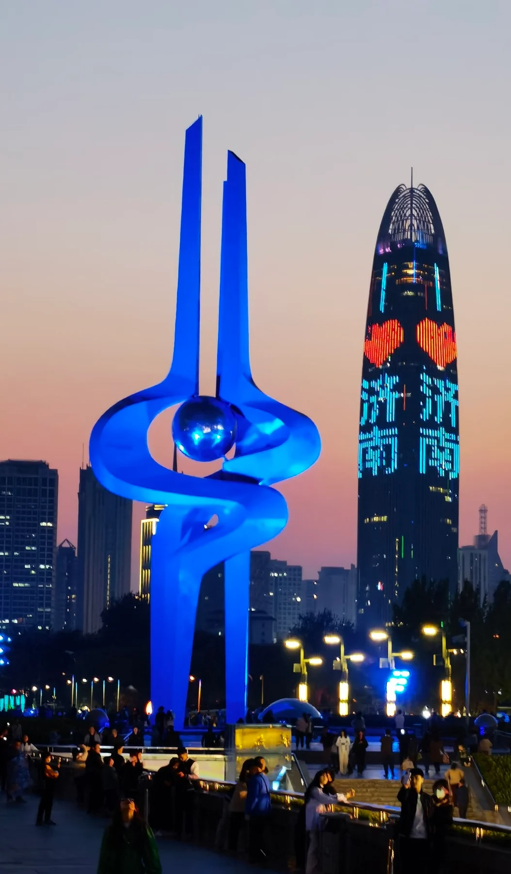 Blue sculpture and illuminated buildings at dusk